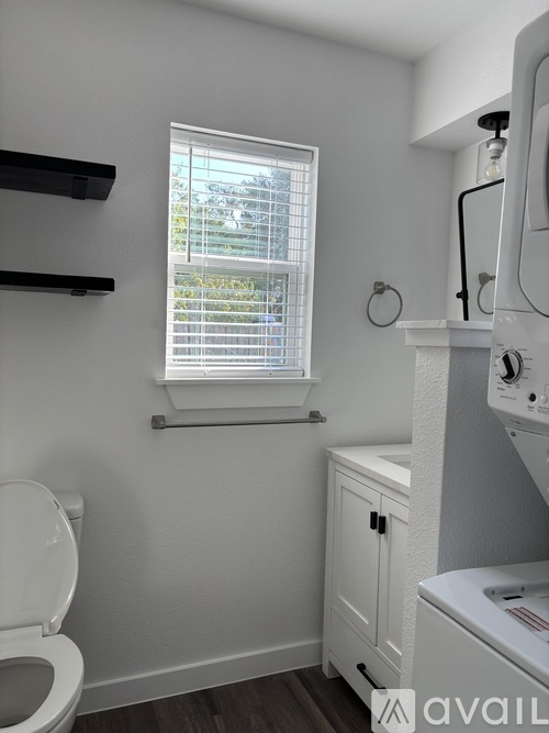 A small bathroom with a toilet, a window with blinds, and a washing machine.