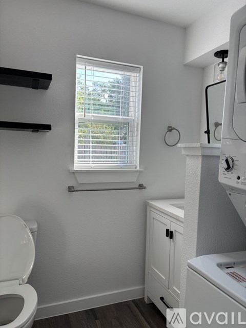 A small bathroom with a toilet, a window with blinds, and a washing machine.
