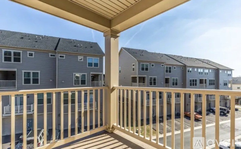 A balcony with a railing overlooks a parking lot and other buildings.