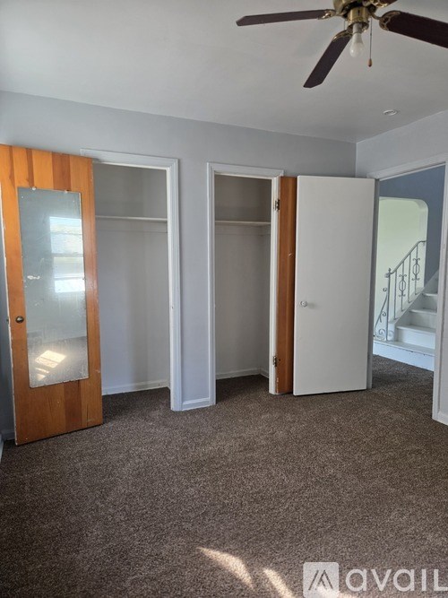 A room with a ceiling fan and three open doors.