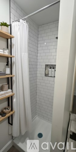 A white shower curtain hangs in a white tiled shower.