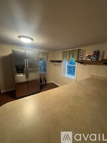 A kitchen with a refrigerator and a window with curtains.