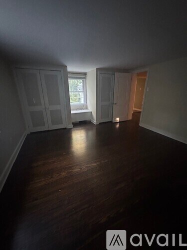 A room with wooden floors and white walls, with a window and a door visible.