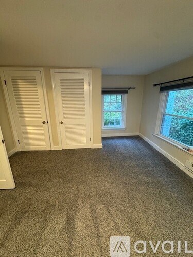 A room with a carpeted floor, two closet doors, and a window with blinds.