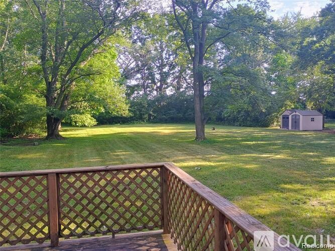 A wooden deck with a lattice fence overlooks a grassy yard with trees.