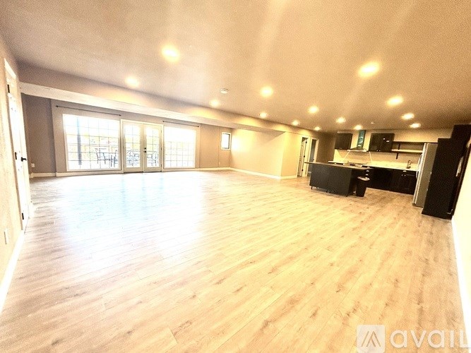 A spacious room with wooden flooring and a kitchen area.