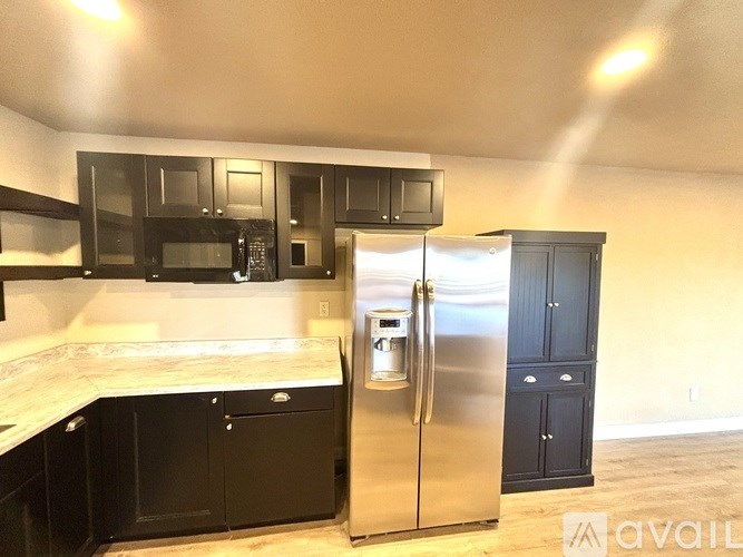 A kitchen with black cabinets and a stainless steel refrigerator.