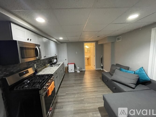 A kitchen with a black stove top oven and microwave, a grey couch, and a wooden floor.