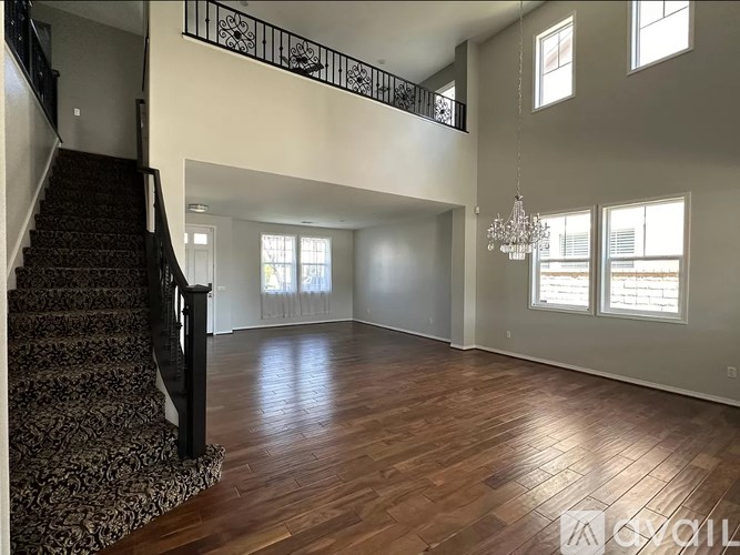 A spacious room with wooden floors and a staircase with a black railing.
