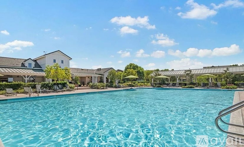 A large swimming pool in the foreground with a house and trees in the background.