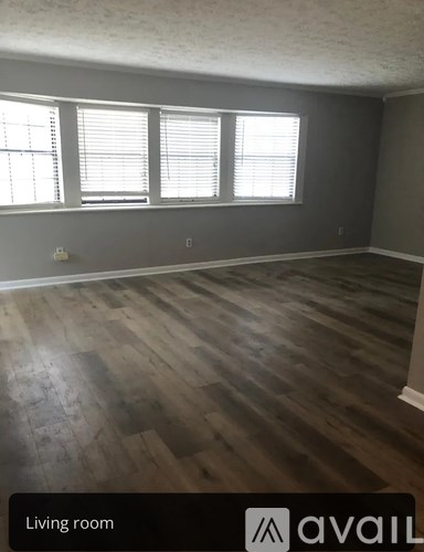 A living room with wooden flooring and a window with blinds.