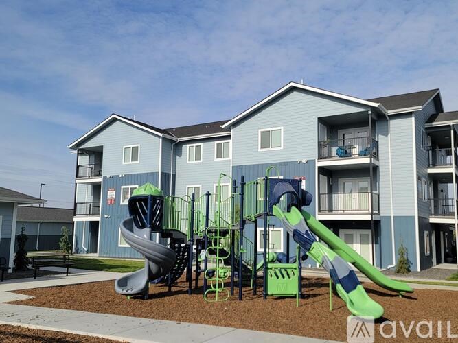 A playground with a green slide and a play structure in front of a blue apartment building.