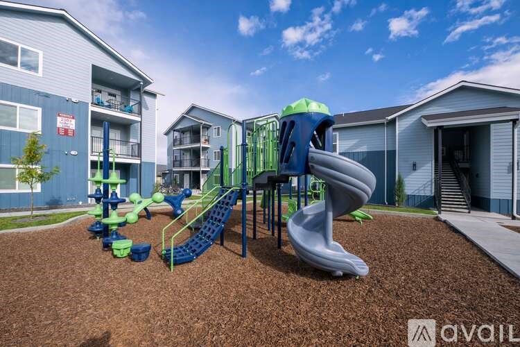 A playground with a blue slide and green climbing frame in front of apartment buildings.