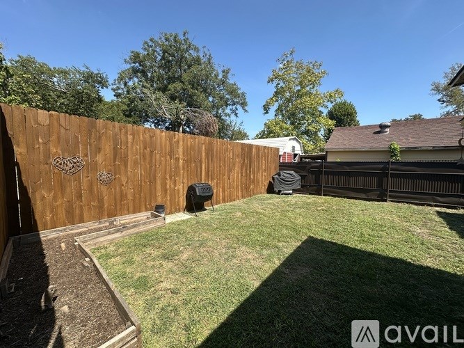 A backyard with a wooden fence and a black grill.