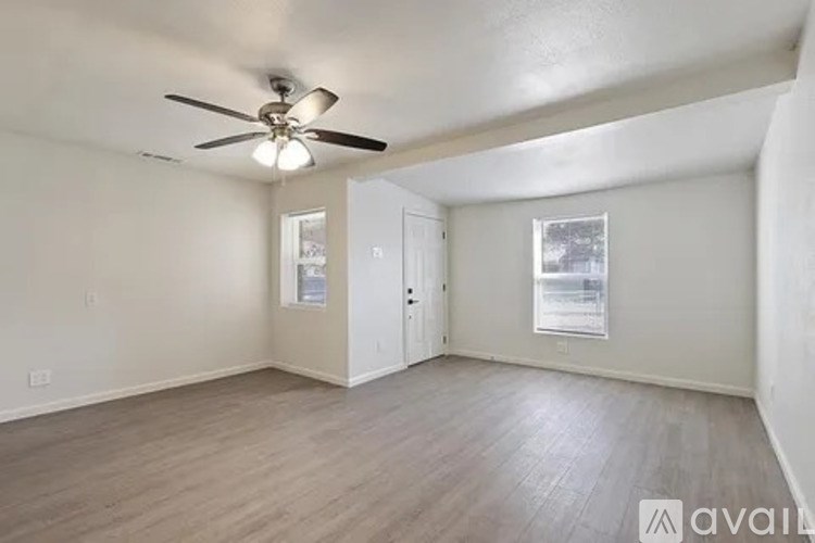 A room with a ceiling fan and light, hardwood floors, and two windows.