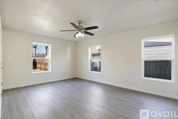A spacious room with a ceiling fan and two windows.