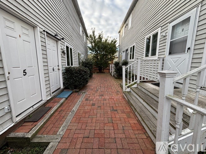 A red brick pathway leads to a white building with numbered doors.