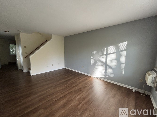 A room with wooden flooring and a staircase in the background.