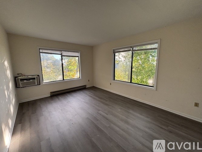 A room with two windows and wooden flooring is available for rent.