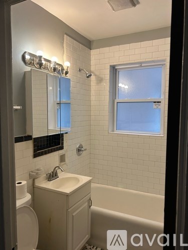 A bathroom with a toilet, sink, mirror, and a window.
