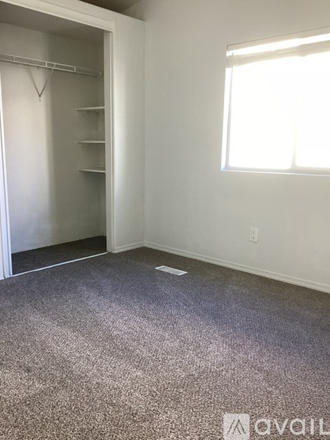 A room with a grey carpet and a white wall with a window.
