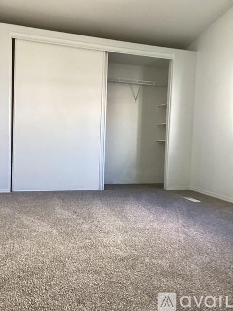 A carpeted room with a white door and a white closet with a shelf.