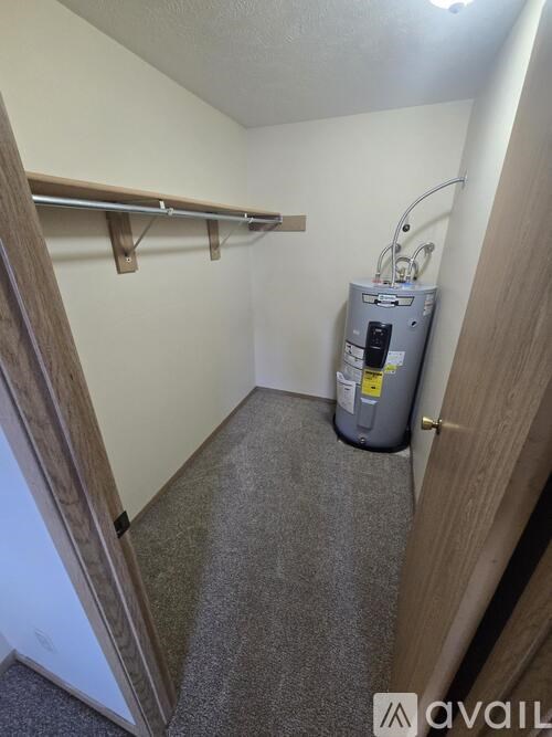A small room with a grey carpet and a grey water heater.