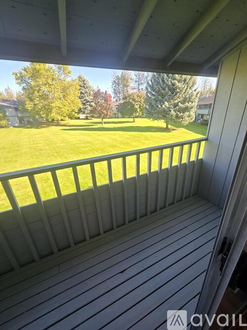 A wooden deck with a view of a green lawn and trees.