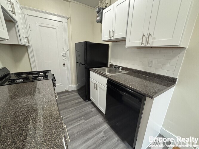 A kitchen with a black refrigerator and white cabinets.