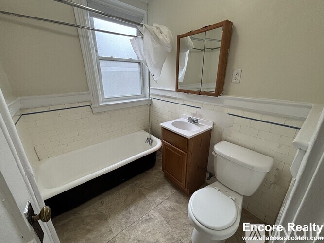 A white toilet sits next to a sink in a bathroom with a tub and mirror.