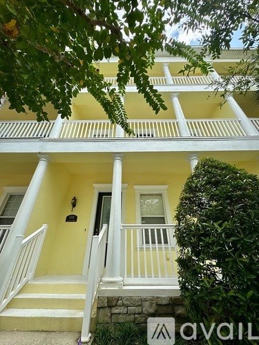 A yellow house with a white porch and a tree in front.