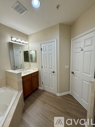 A bathroom with a tub, sink, mirror, and two doors.