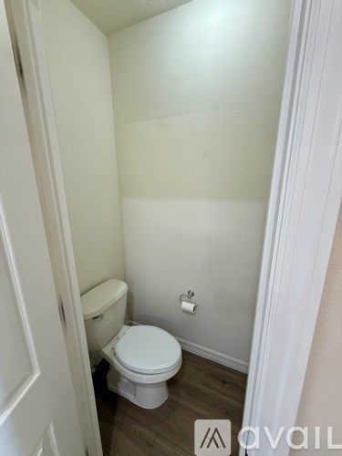 A white toilet in a small bathroom with wood flooring.