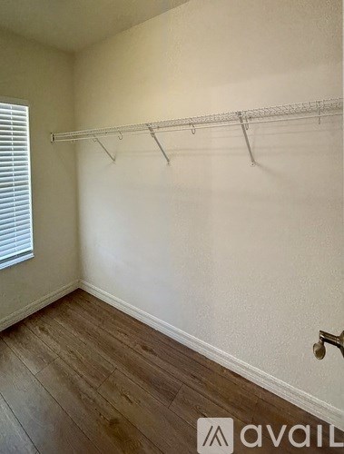 A room with a wooden floor and a white wall with a coat rack.