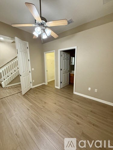 A room with a ceiling fan and light fixture, wooden flooring, and a staircase with white railings.