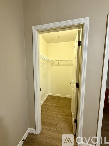 A white door is open to a small, empty room with wooden flooring.