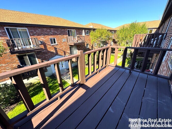 A wooden deck with a railing and a building in the background.