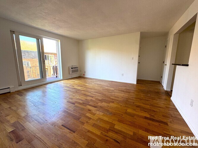 A room with wooden flooring and a window overlooking a building.