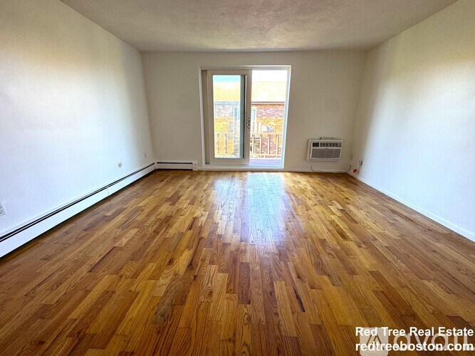 A room with wooden flooring and a window overlooking a cityscape.