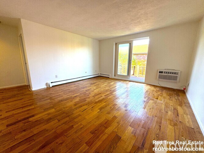 A room with wooden flooring and a window overlooking a building.