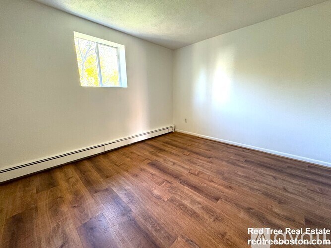 A room with wooden flooring and a window letting in sunlight.
