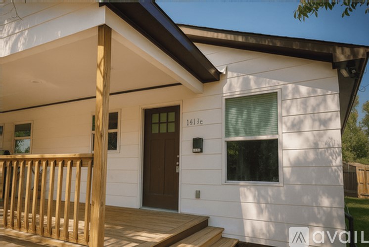A white house with a brown door and a window with green blinds.