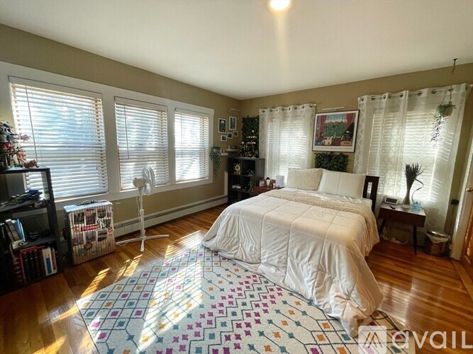 A bedroom with a bed, a chair, a bookshelf, and a window with blinds.
