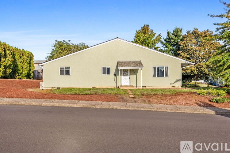 A house with a white door and windows is surrounded by greenery and a red brick wall.