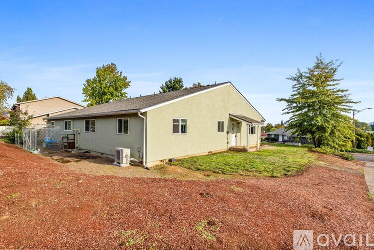 A two-story house with a brown roof and a white exterior is surrounded by a red mulch area.