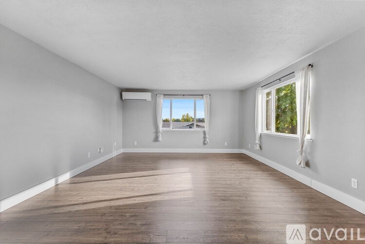 A spacious room with wooden flooring and two windows.
