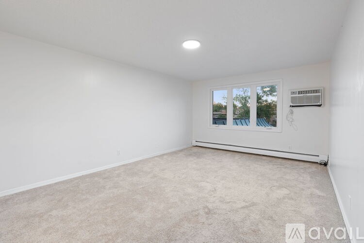 A white room with a carpeted floor and a window showing a view of trees and a building outside.