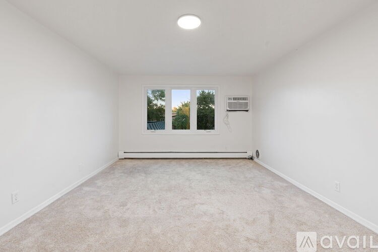 A spacious empty room with a window and a carpeted floor.