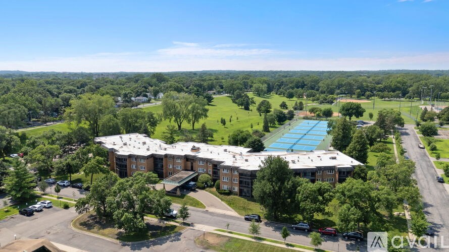 An aerial view of a large building with a swimming pool surrounded by trees and a parking lot.