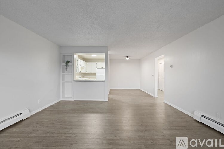 A spacious room with wooden flooring and white walls, with a mirror on the wall reflecting another room.